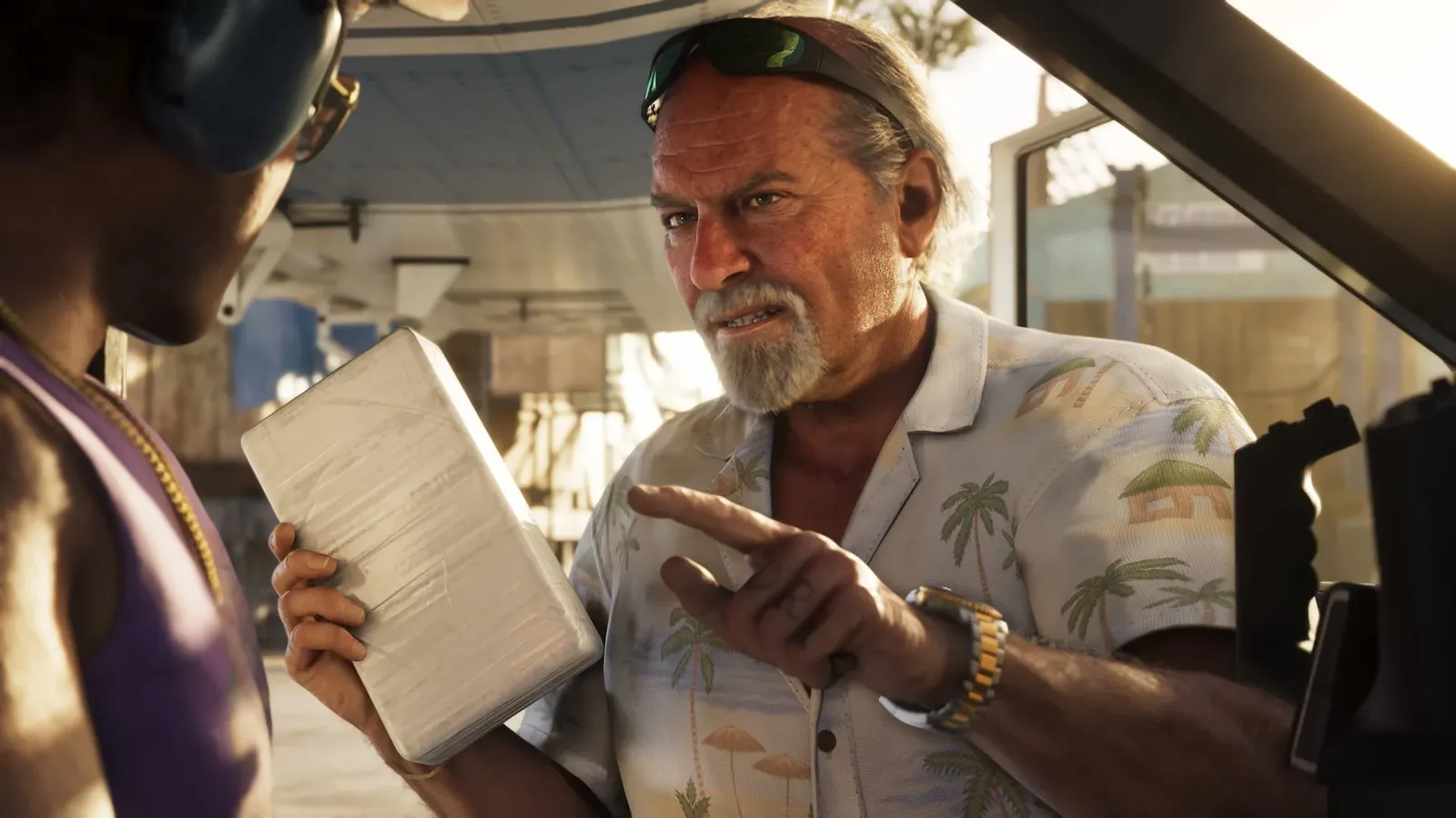 Brian Heder holds a wrapped rectangular package while speaking to a man in a vehicle.
